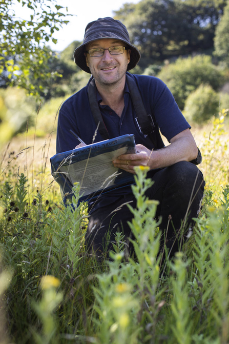 Andy Karran smiling with a clip board amongst plants